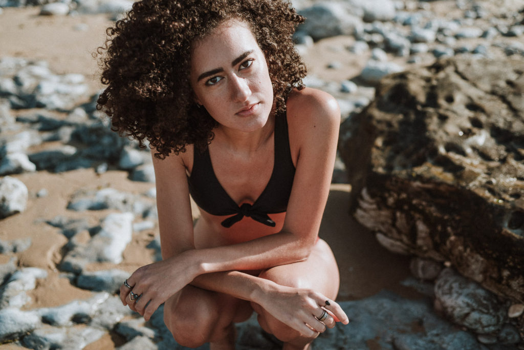fashion photographer praia da parede - girl sitting on rock with black and red bikini looking at camera