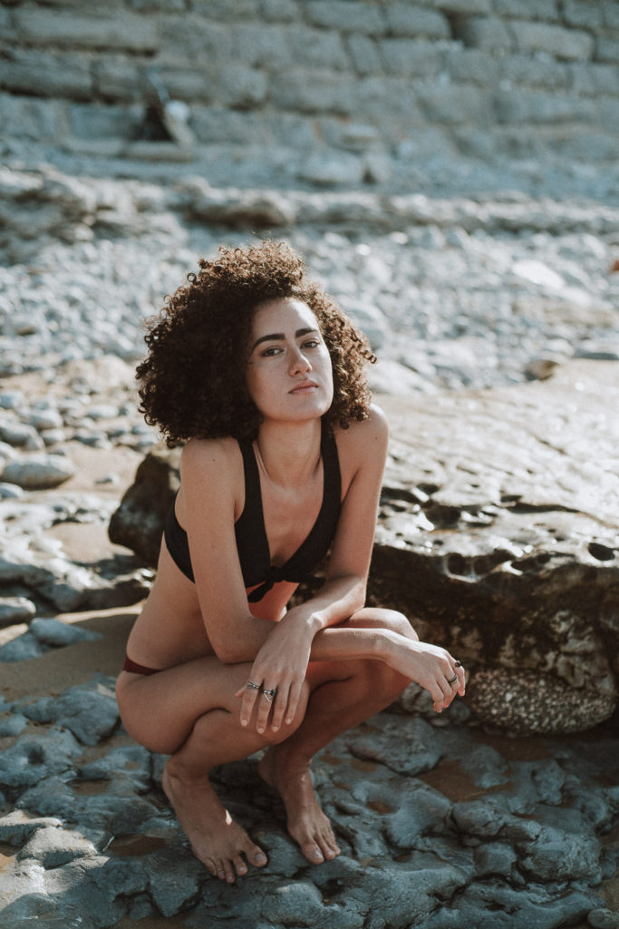 fashion photographer praia da parede - girl sitting on rock with black and red bikini looking at the sea